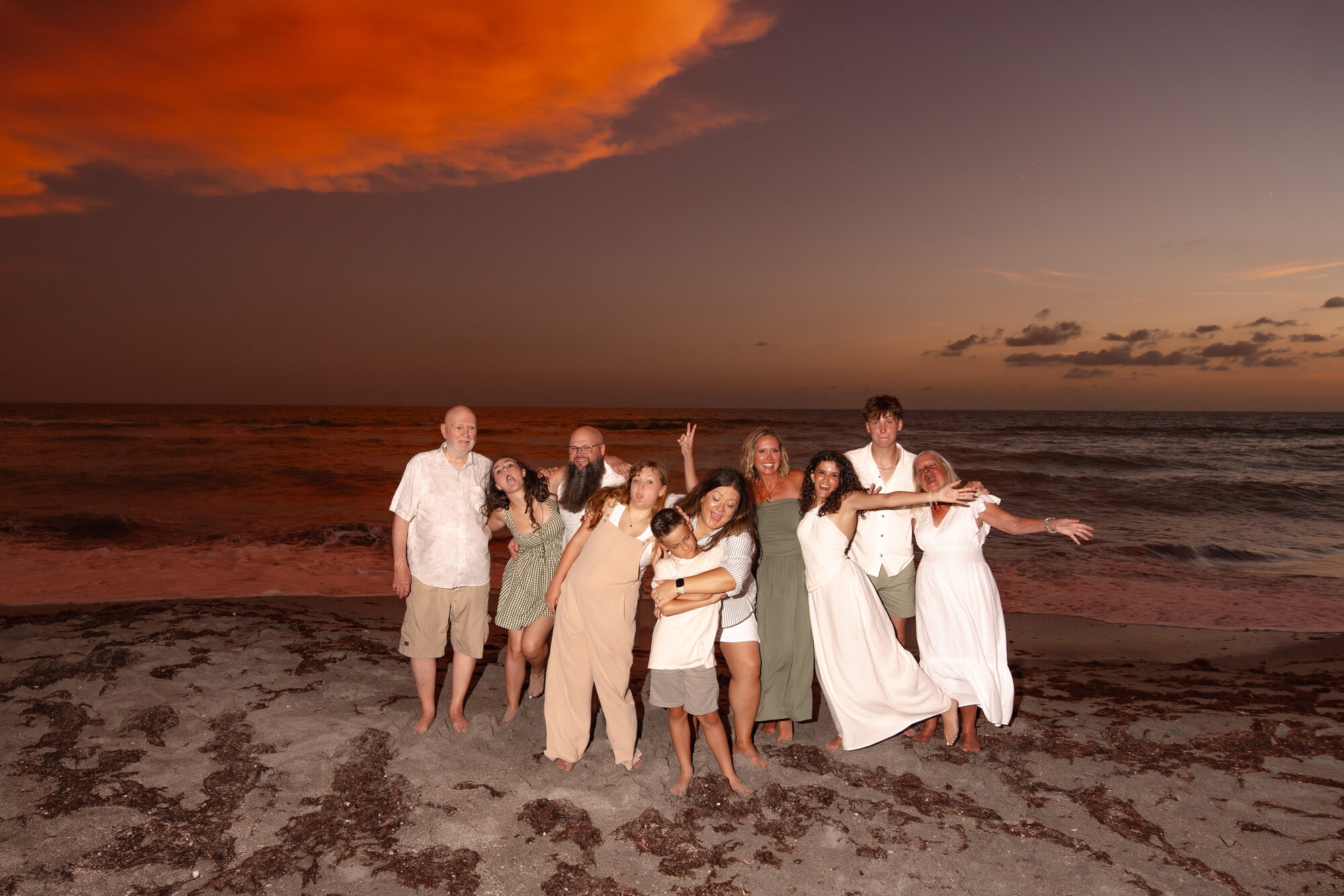 Multi-generational family portrait on the beach under a fiery sunset sky
