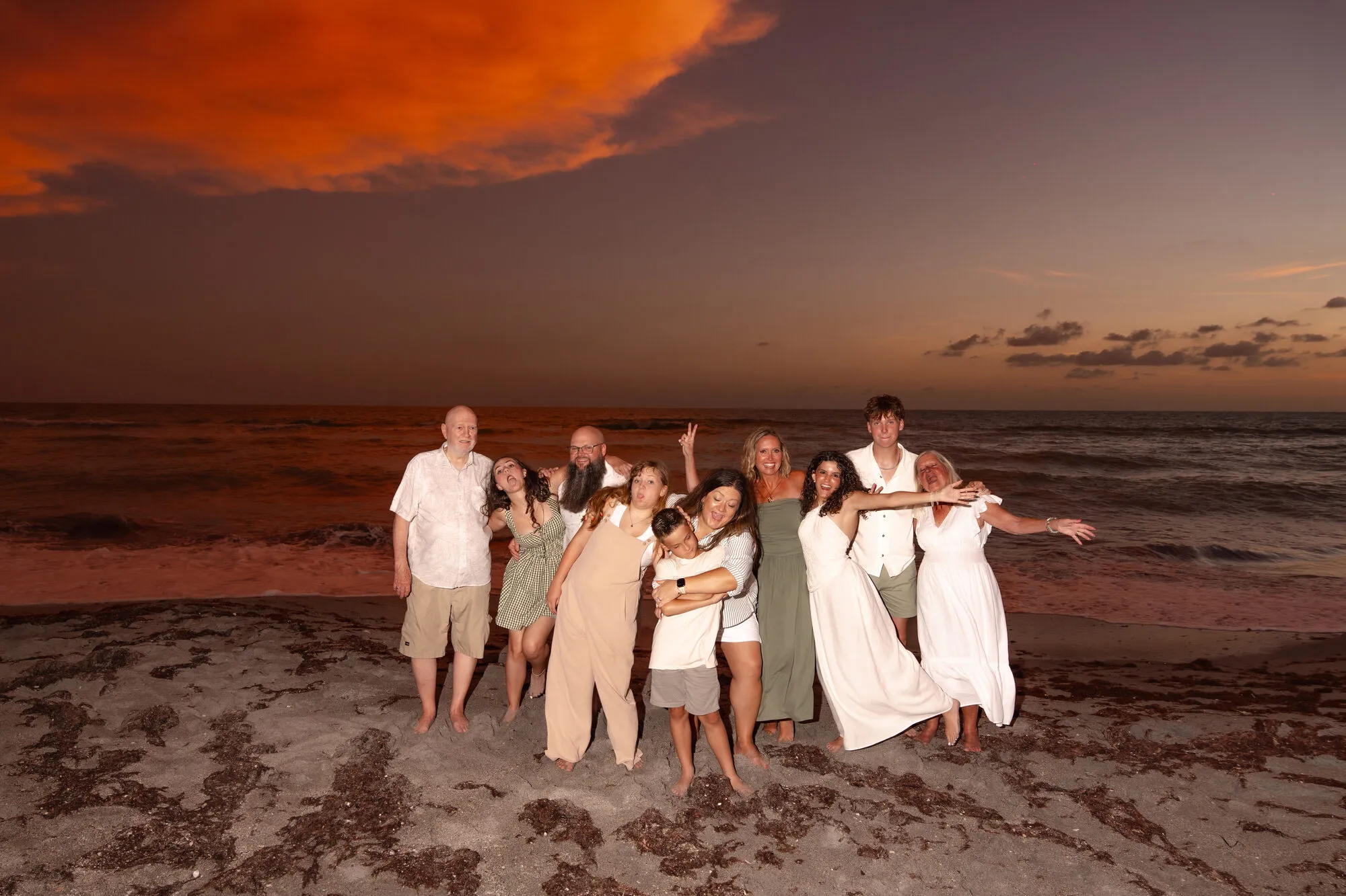 Multi-generational family portrait on the beach under a fiery sunset sky