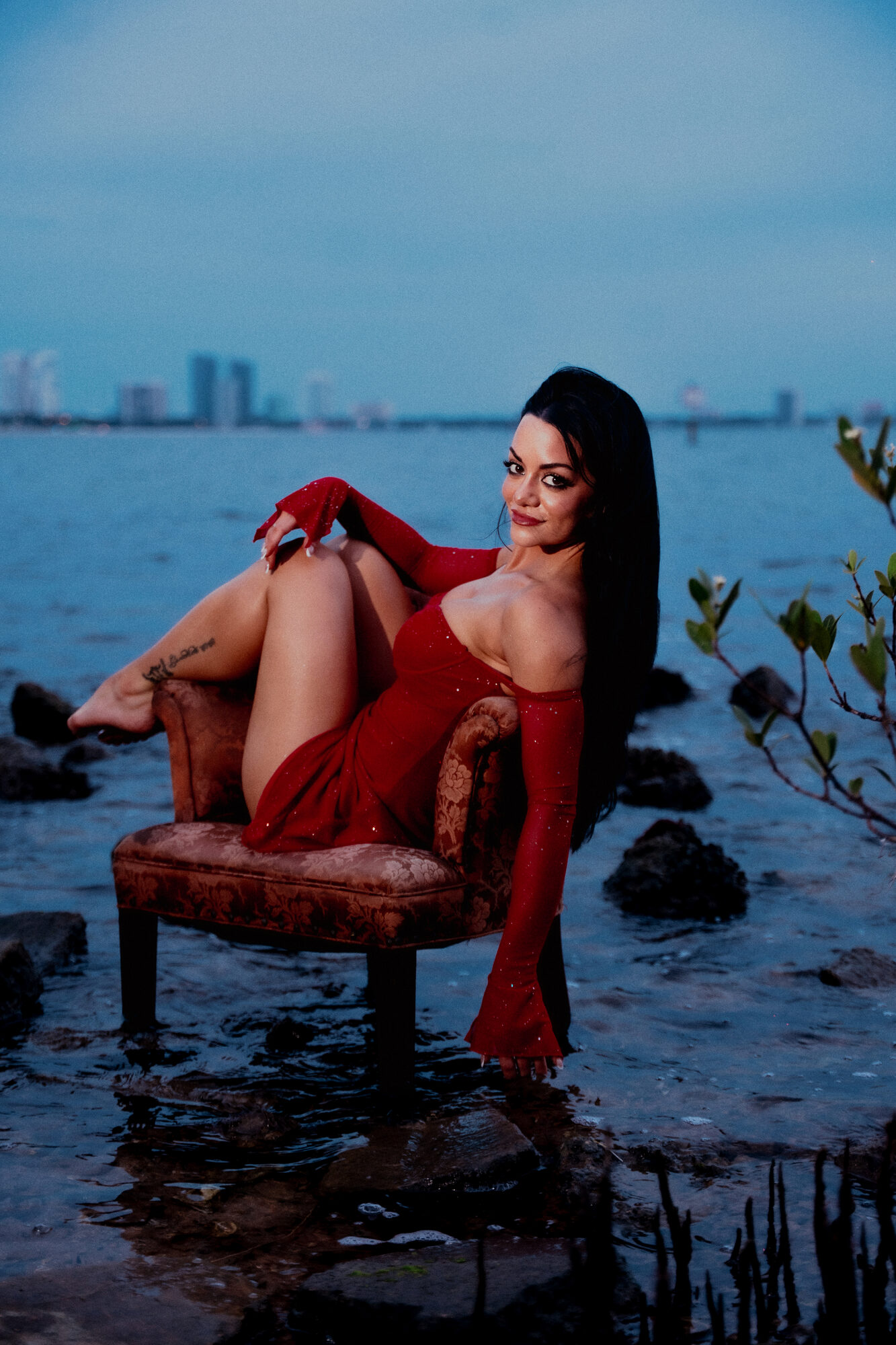 Editorial portrait in a red dress on a vintage chair in the bay at dusk