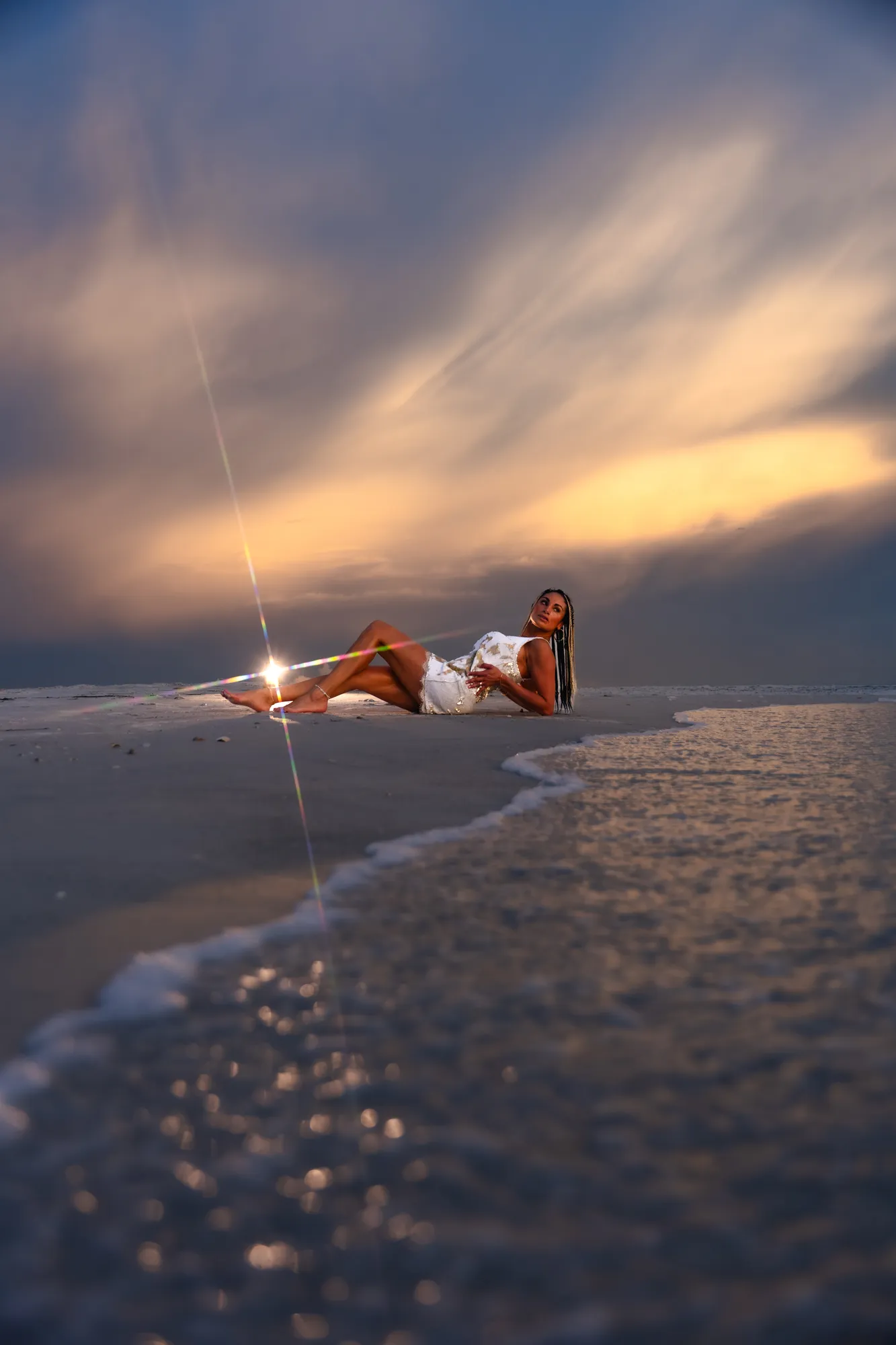 Wide editorial portrait lying on the shoreline beneath a dramatic sunset sky