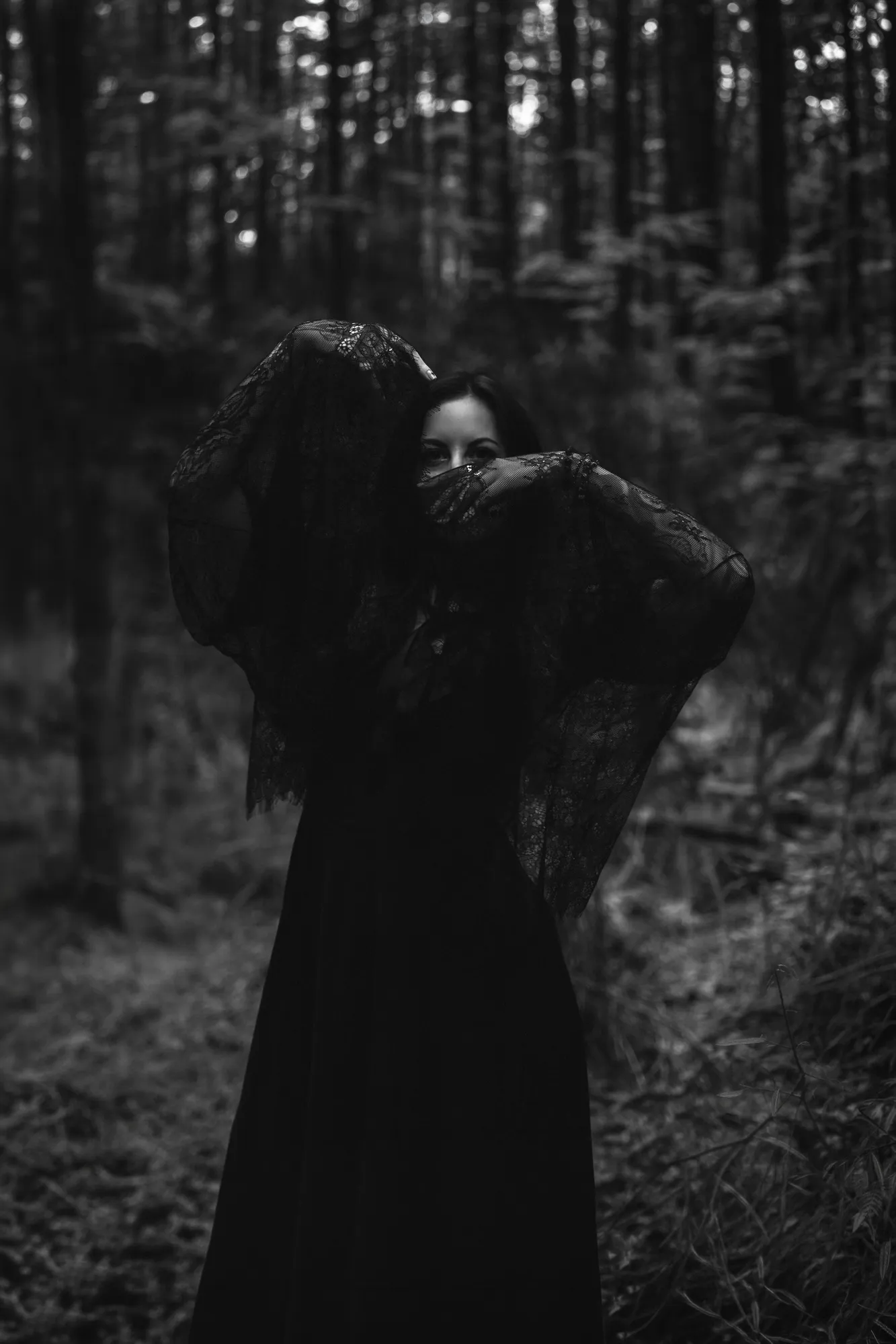 Black and white fine-art portrait in a black lace veil deep in the pine forest